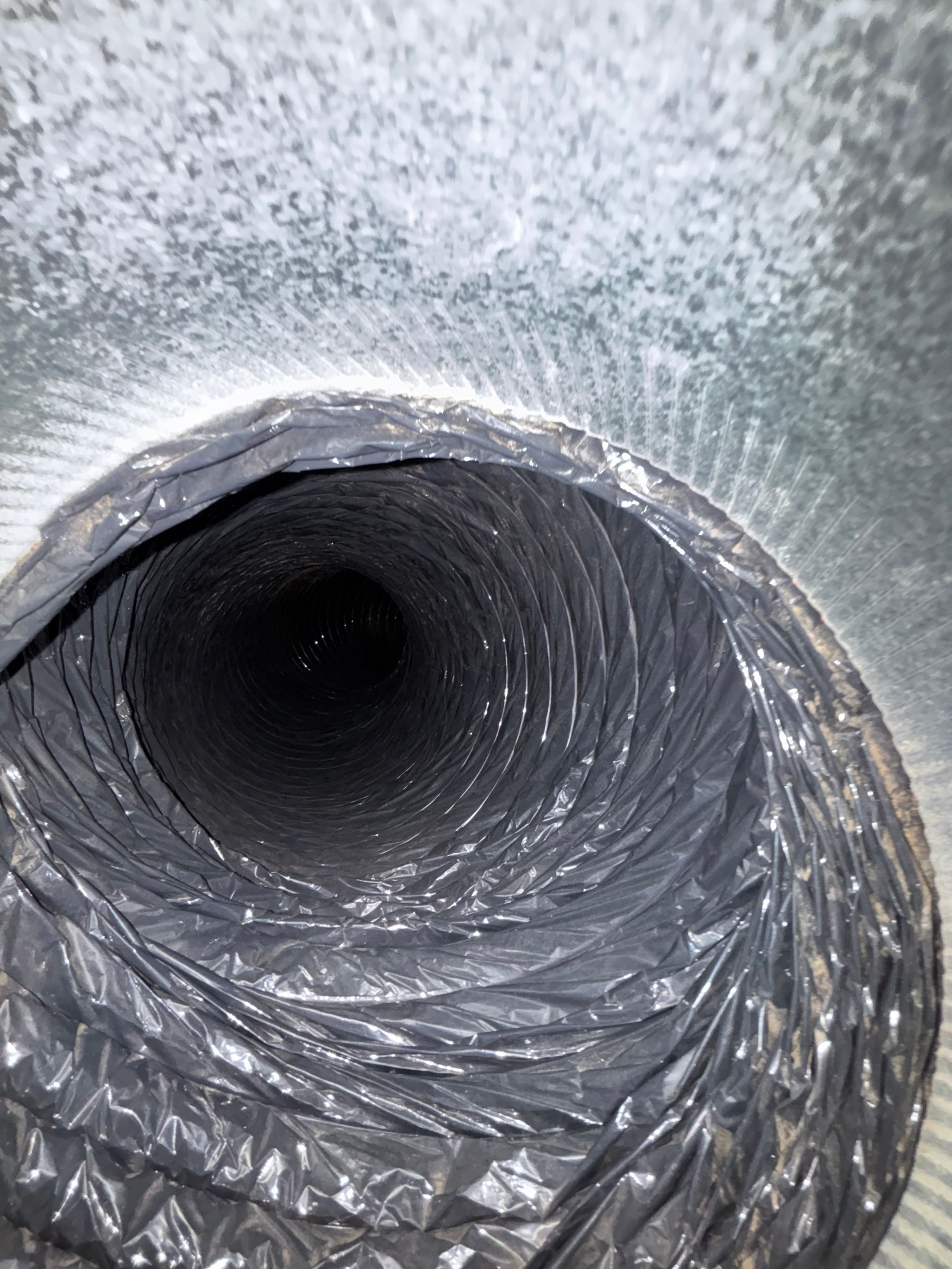 Inside a metallic air duct with reflective, crinkled insulation lining the tunnel