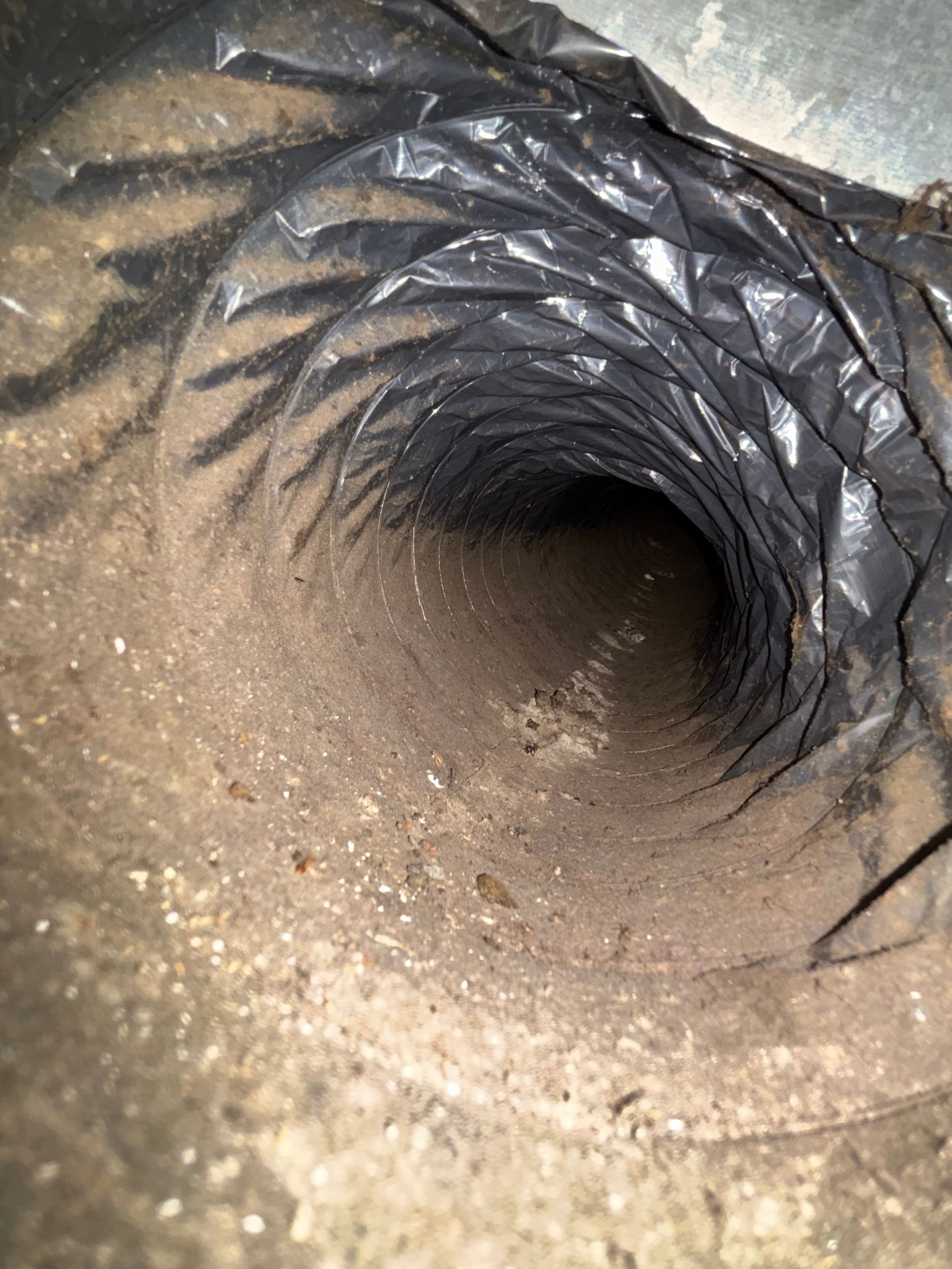 Looking down a narrow, dusty black vent or pipe interior with a dark opening