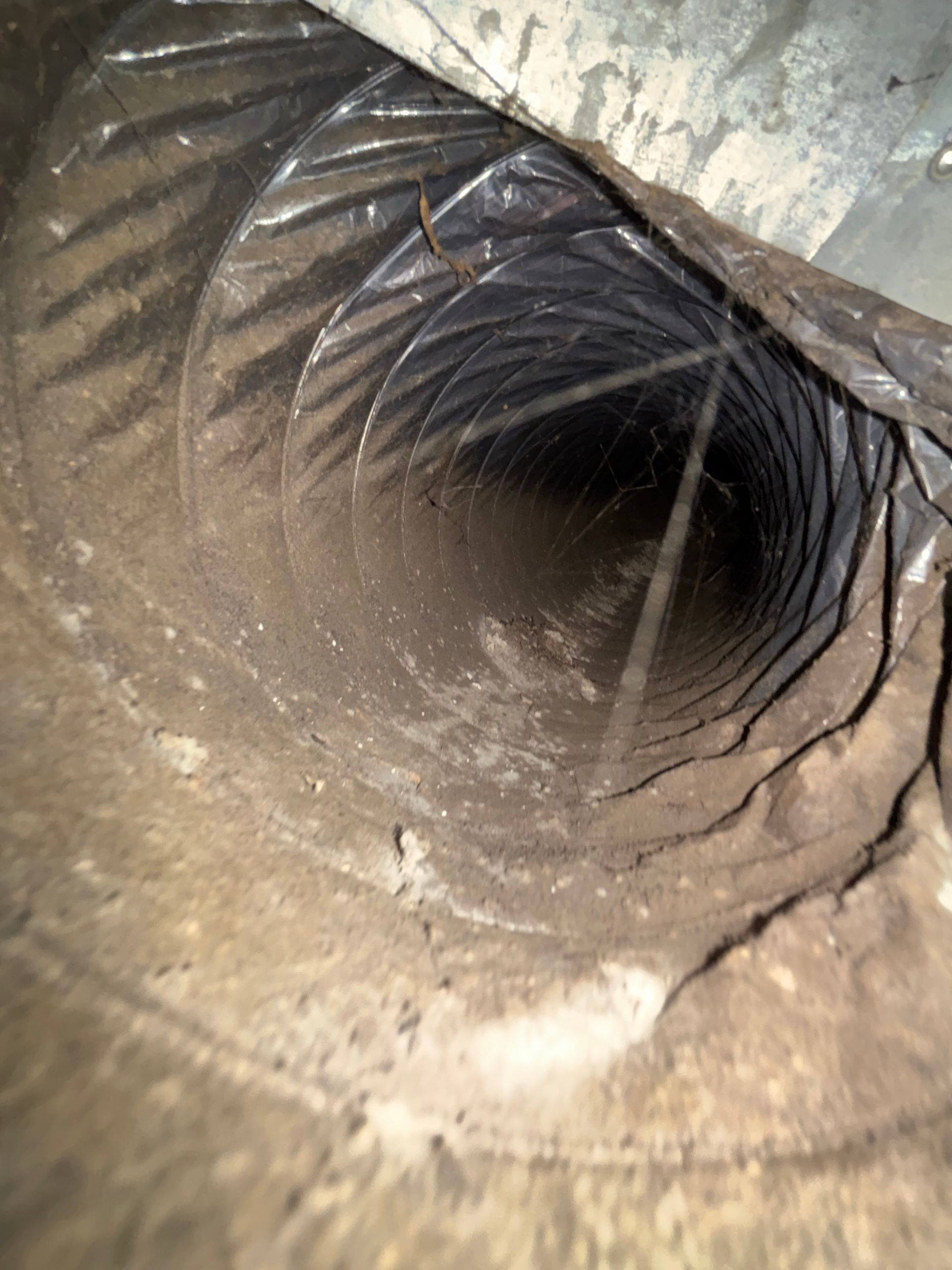 Inside of a dusty metal pipe with ridged, circular walls and a dark tunnel opening