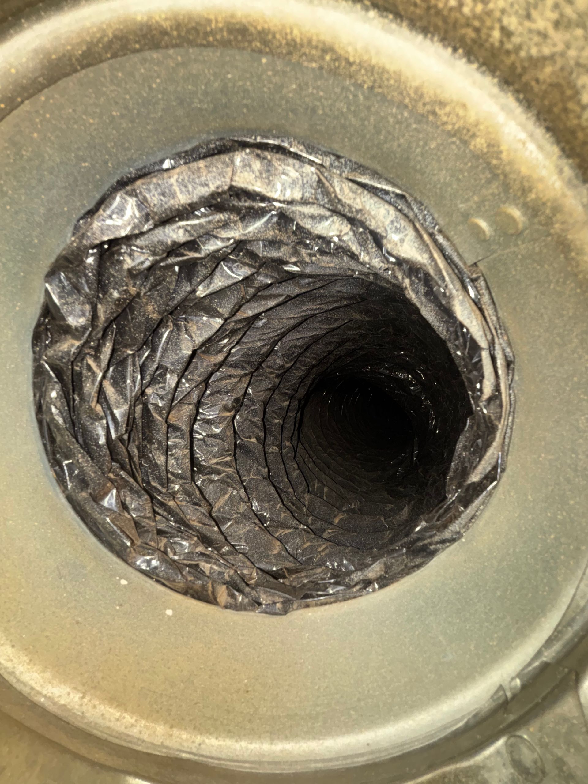 Close-up of a circular metal pipe opening with rough, jagged inner walls and a dark center
