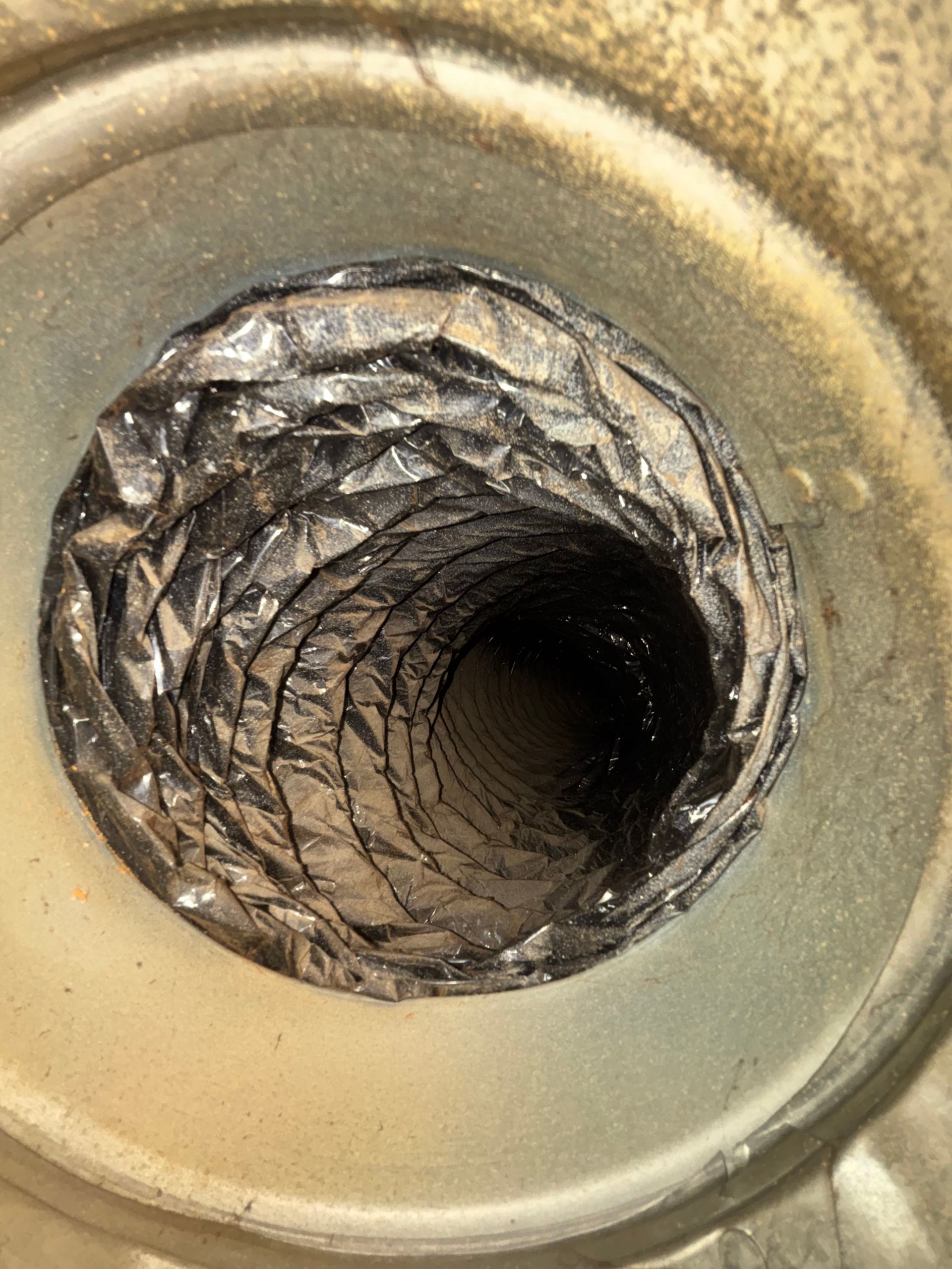 Close-up of a metal duct opening with crumpled, textured foil lining and a dark center.