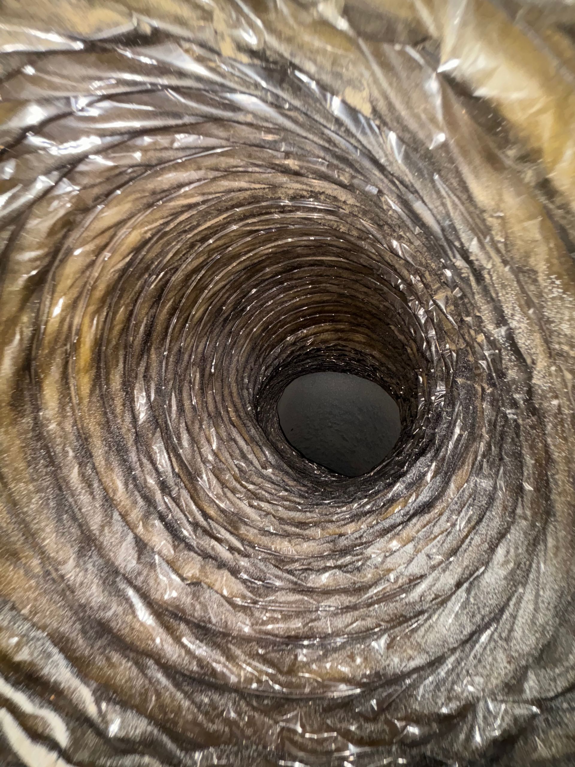 Close-up view down a spiral metallic duct with a dark central opening
