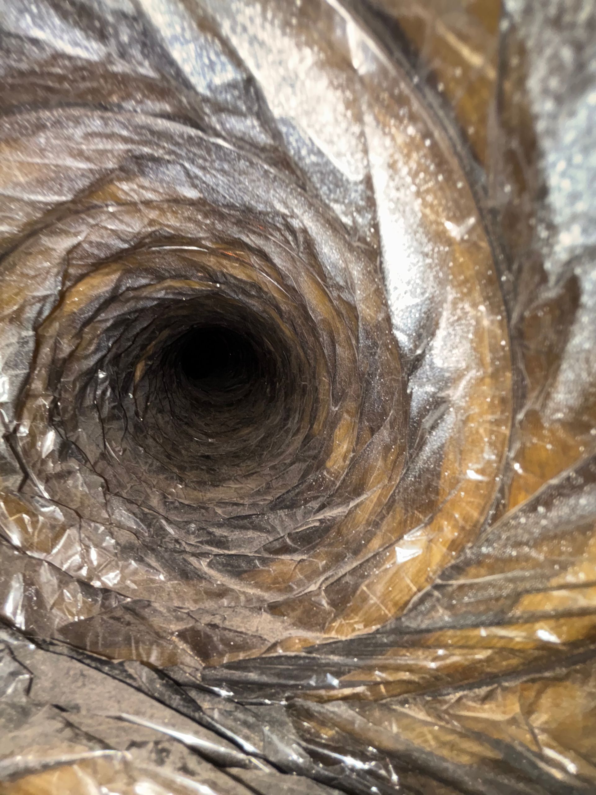 Close-up of a dark, cylindrical tunnel lined with crumpled brown and silver material
