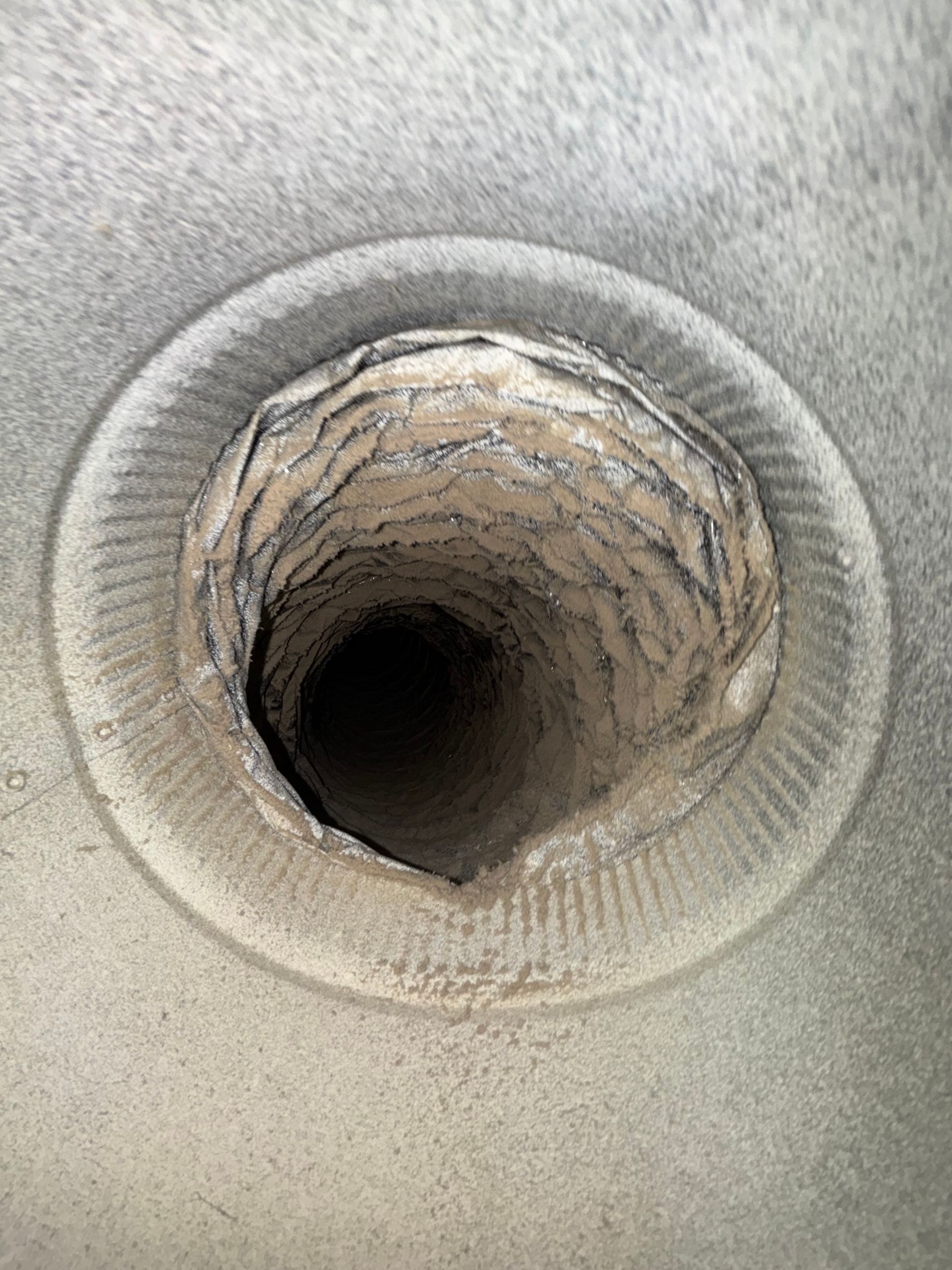 Close-up of a circular vent or pipe opening with a rough, worn interior against a gray surface