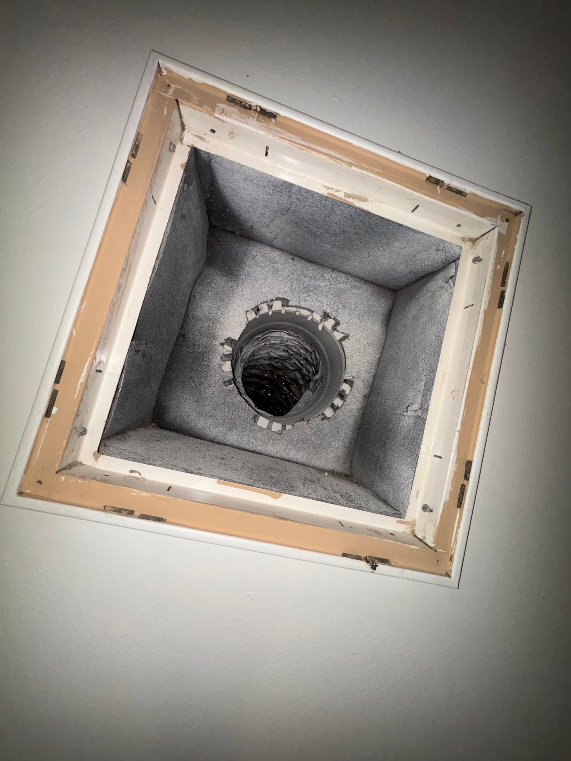 Square ceiling vent opening with exposed duct and gray insulation, viewed from below
