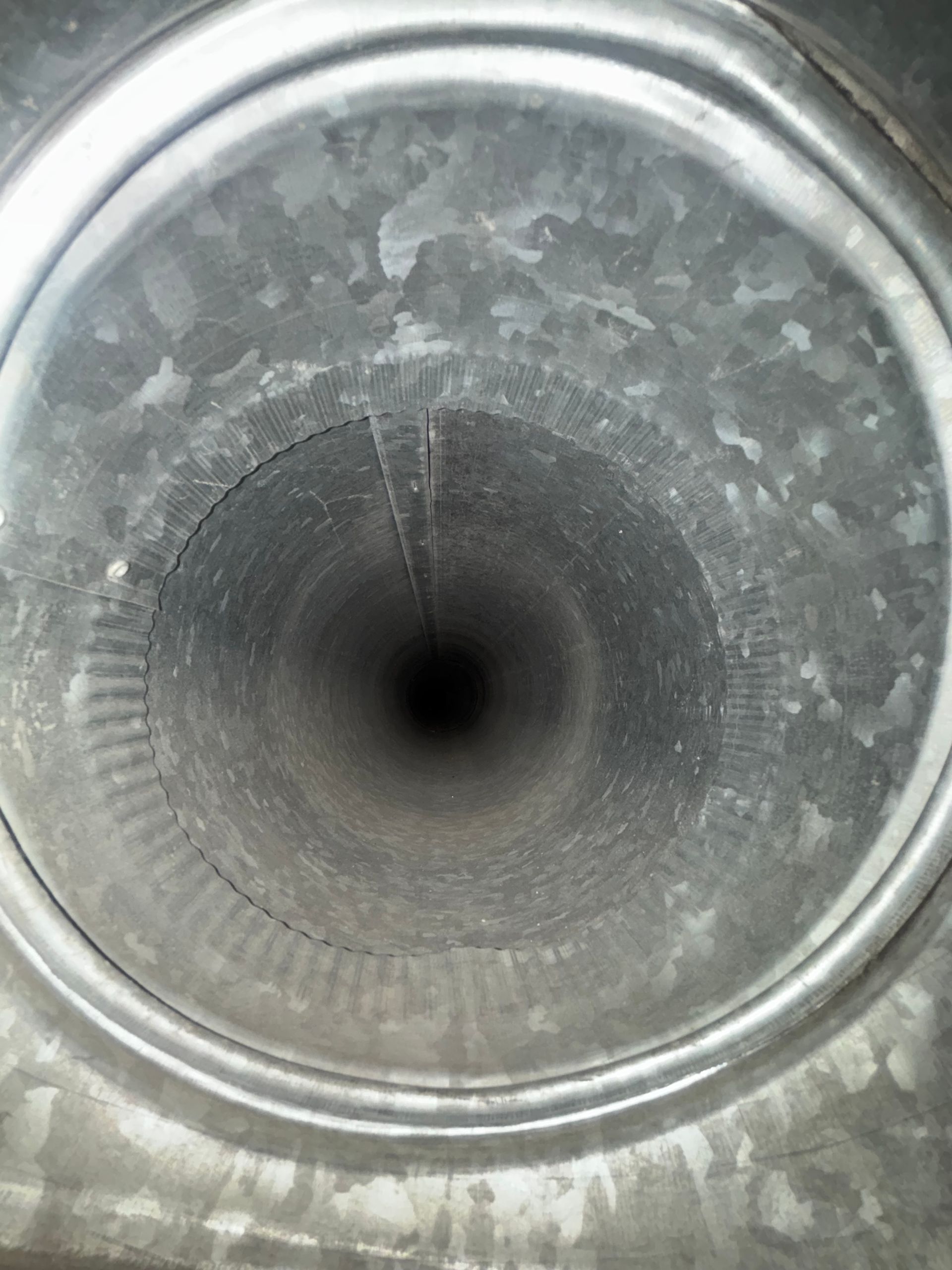 Top-down view inside a metal cylindrical duct with a dark center and water spots.