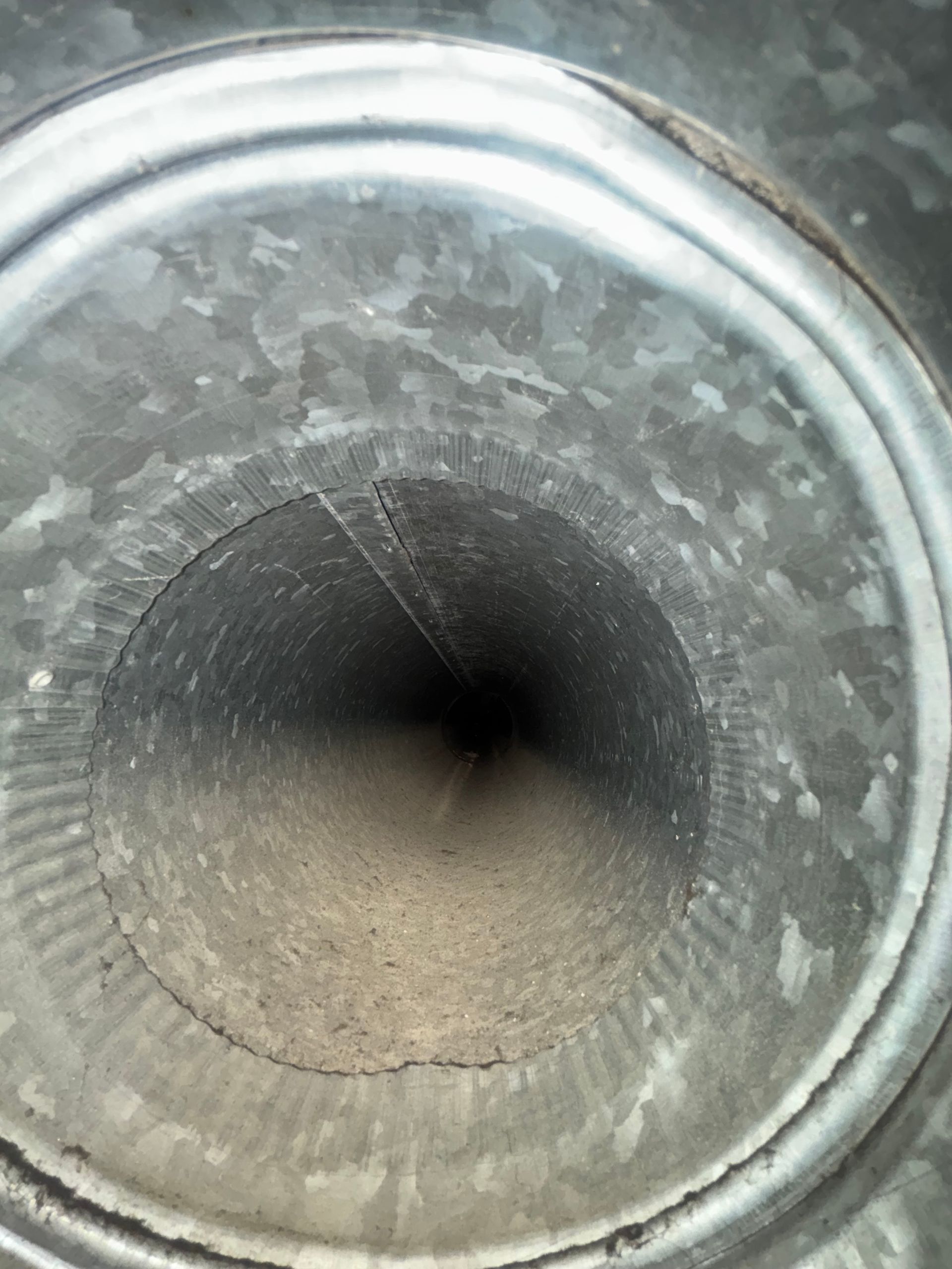 Close-up of a metal funnel or pipe opening with a dark center and worn, scratched surface