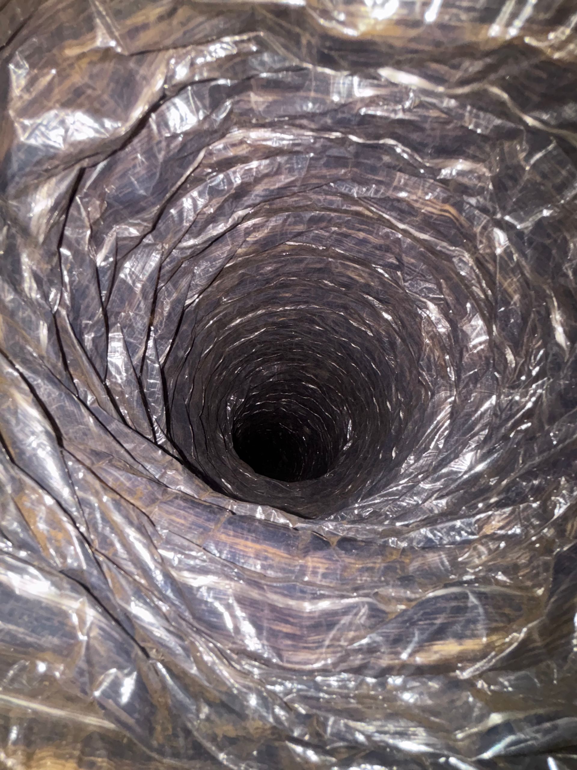 Crumpled plastic-lined tunnel or pipe with a dark circular opening at the center