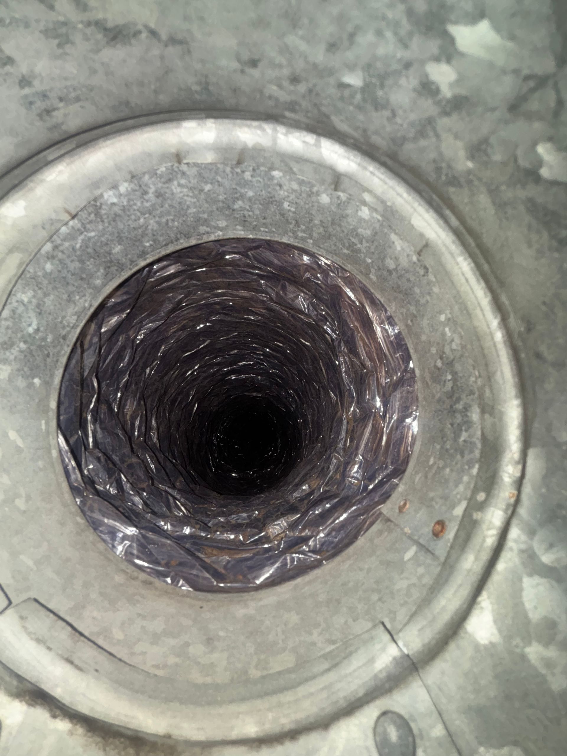 Circular metal opening with a dark, lined pipe or vent inside