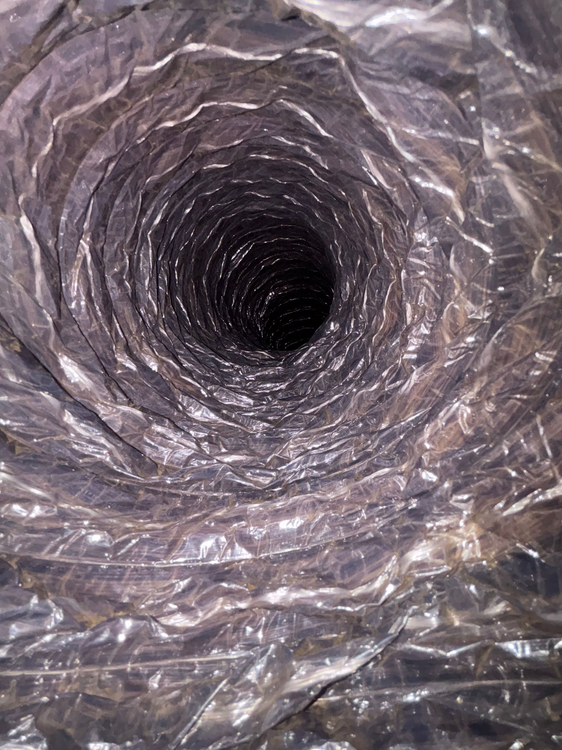 Inside view of a silver metal duct or ventilation pipe leading into darkness