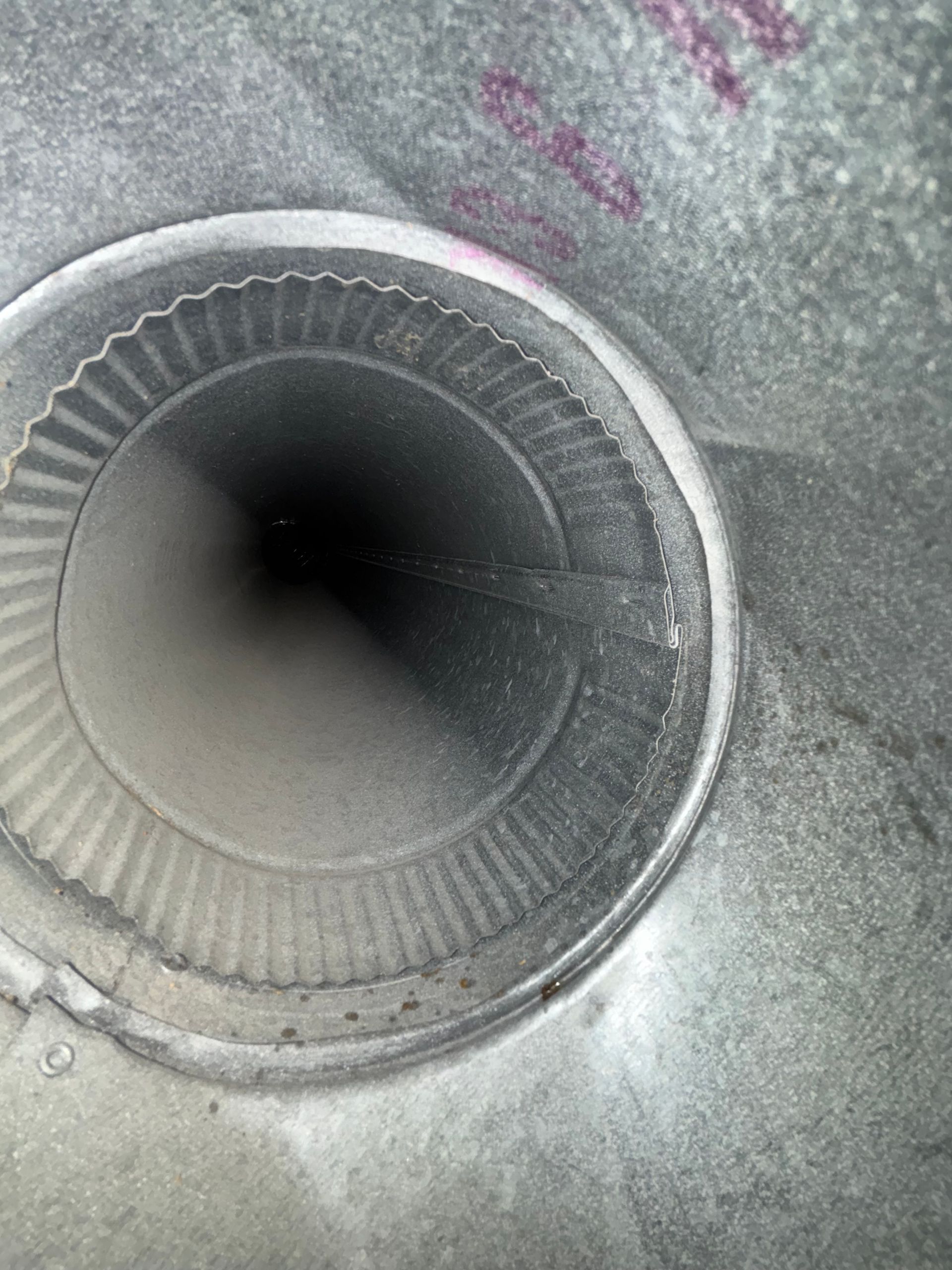 Close-up of a circular metal drain or vent opening on a gray surface.