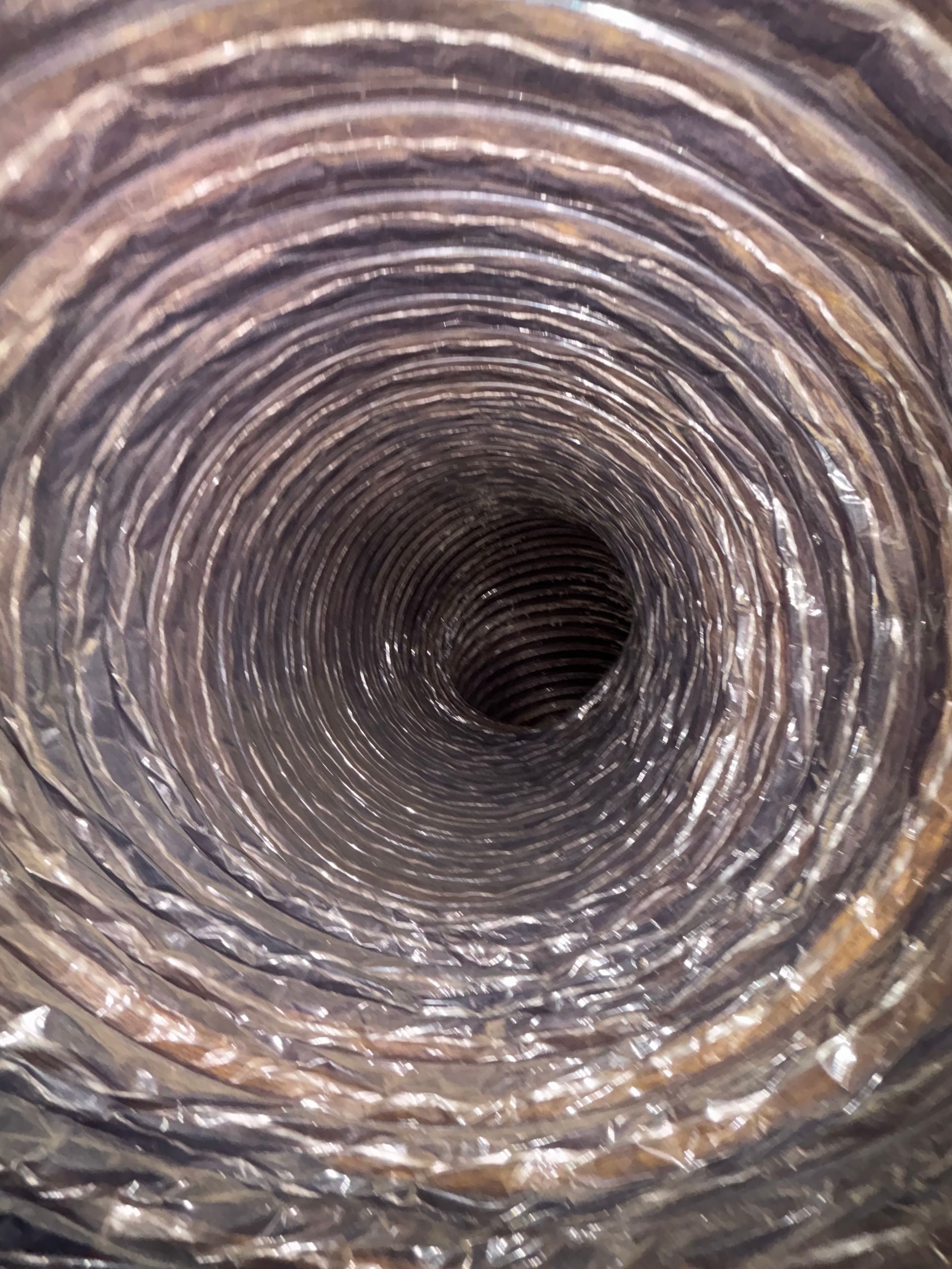Close-up view down a coiled metal hose or duct with a dark tunnel center