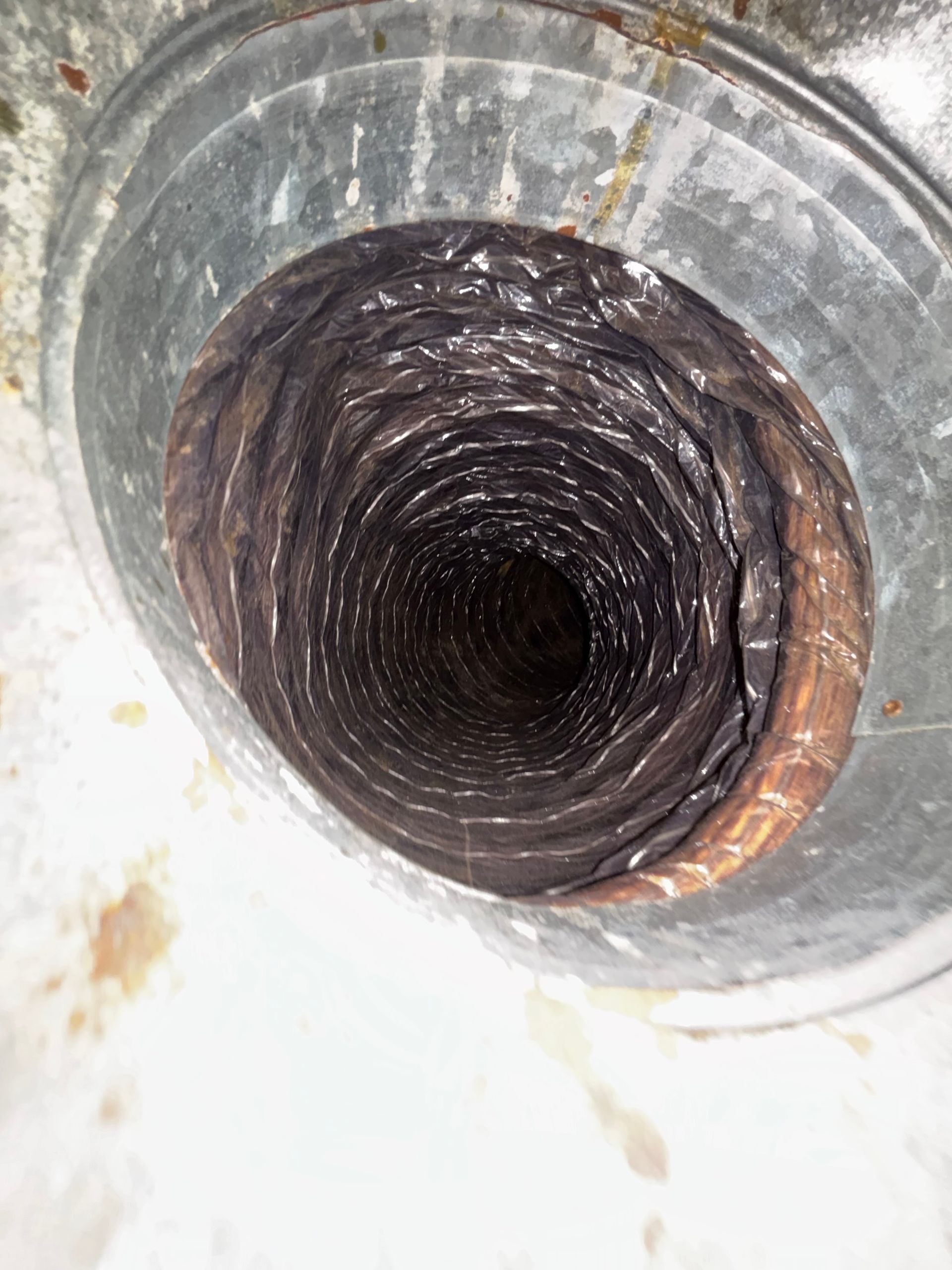 Close-up of a dark, coiled pipe or duct opening inside a white metal surface