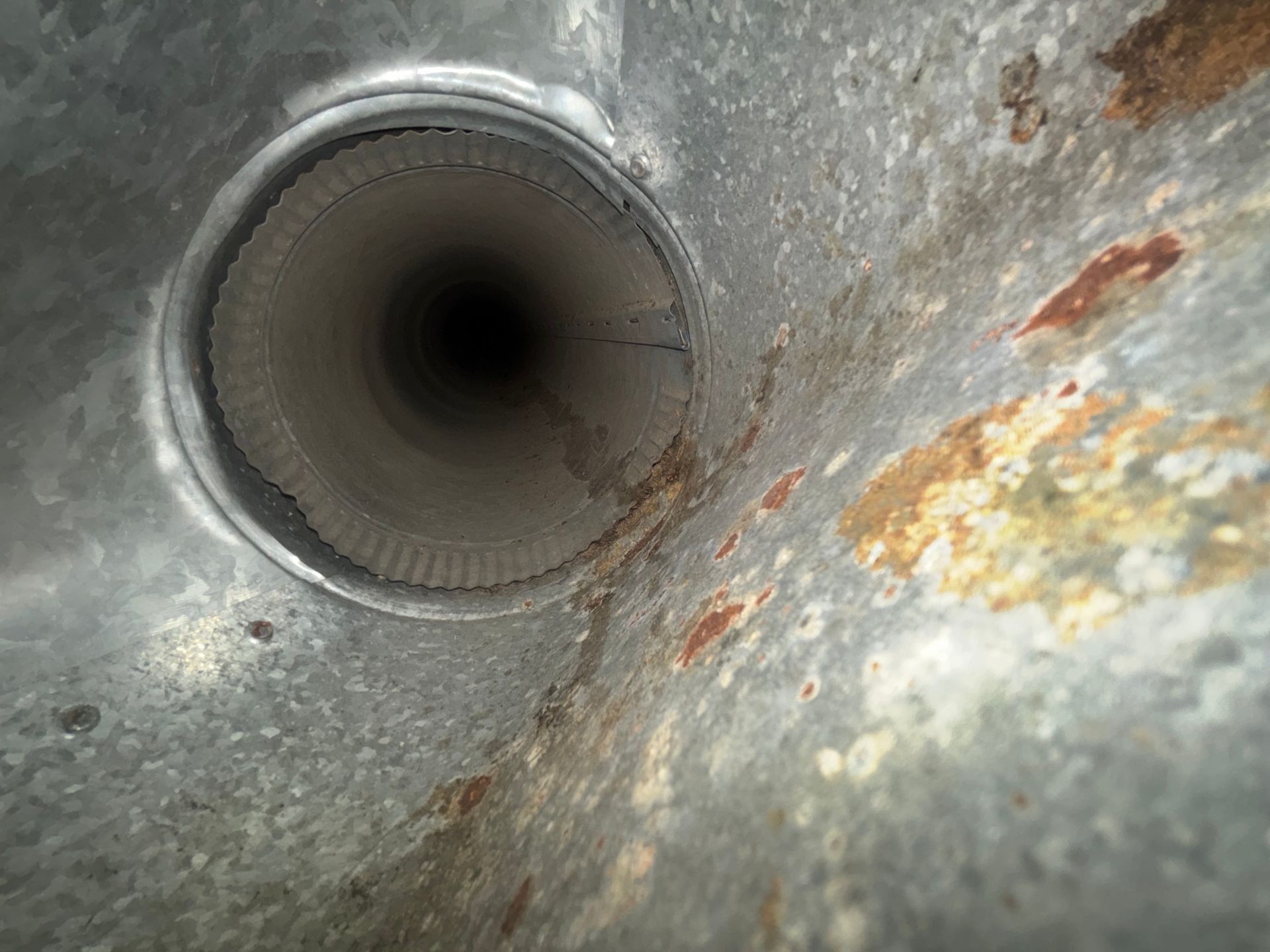 Close-up of a metal pipe opening with rust and corrosion on the surrounding surface