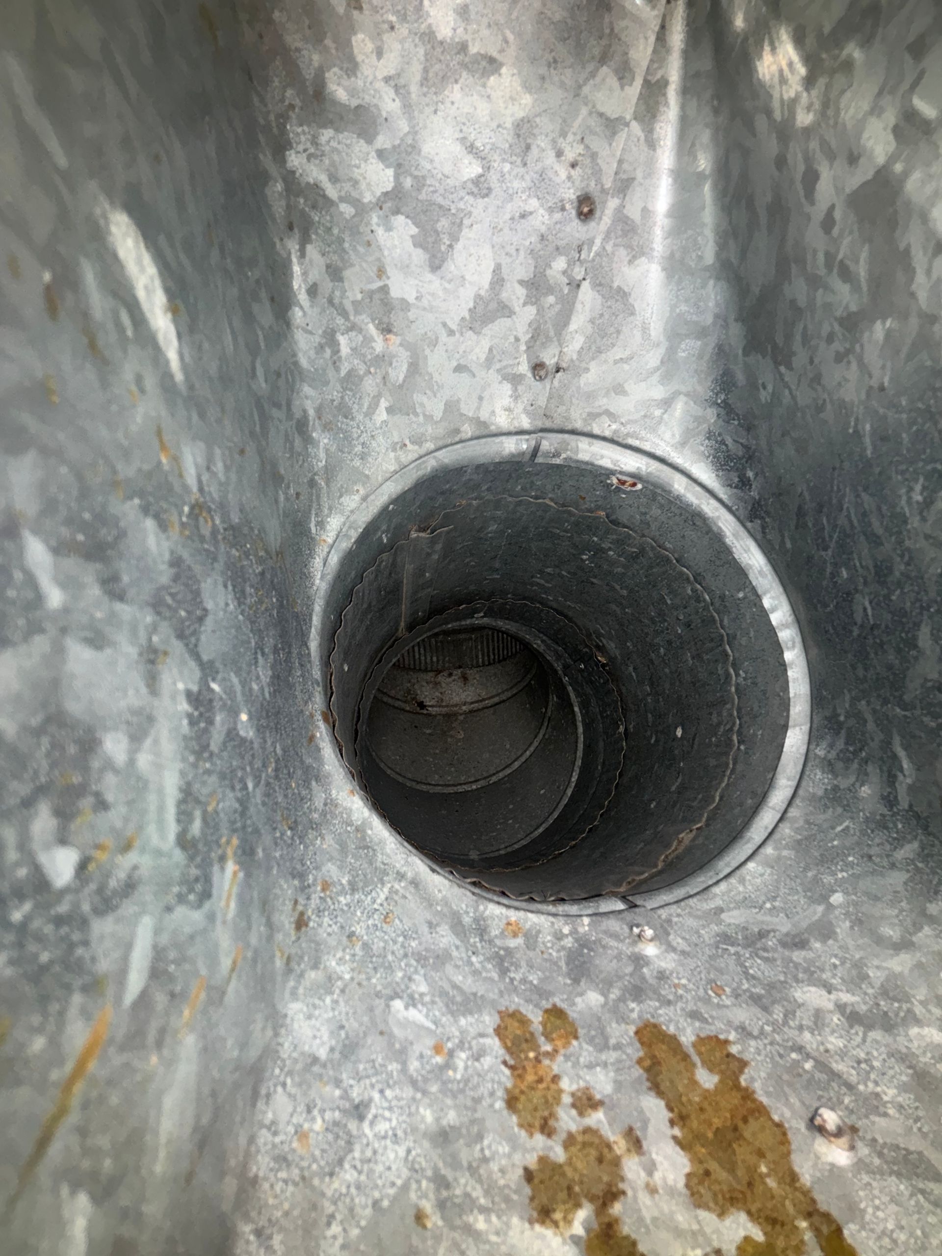 Close-up of a gray metal pipe opening with rust stains on the surrounding surface.