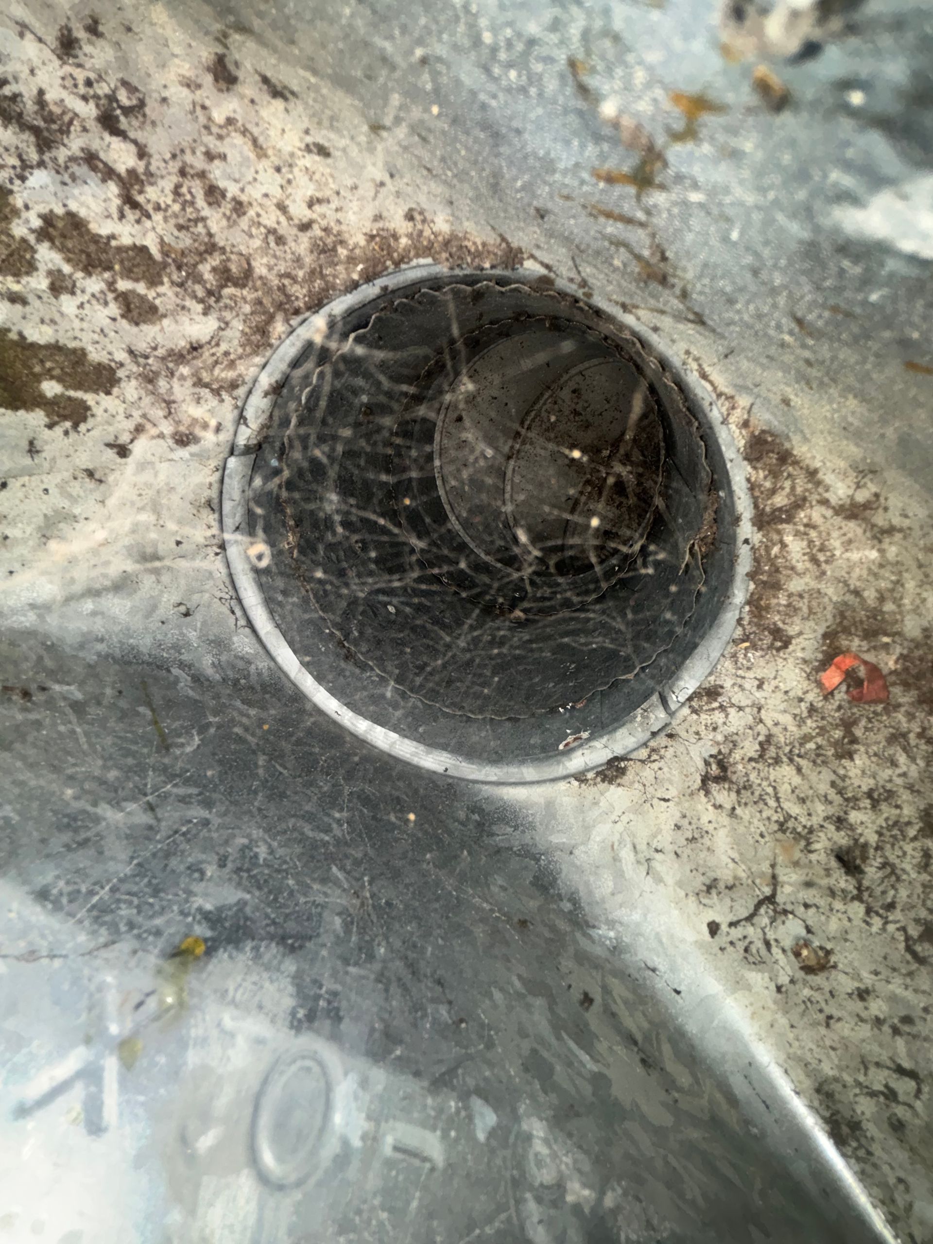 Close-up of a dusty metal surface with a circular pipe opening filled with cobwebs