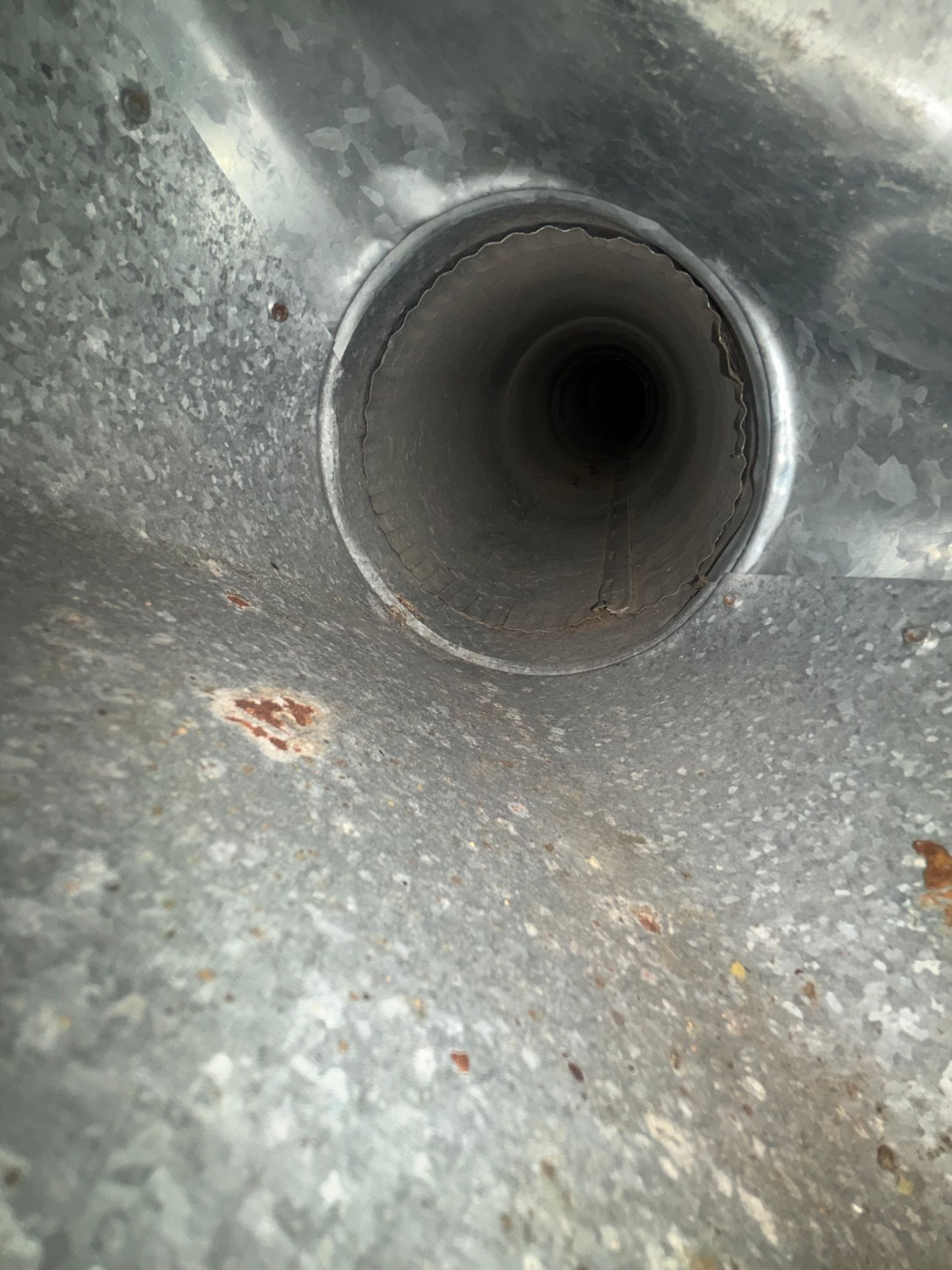 Close-up of a dark circular pipe opening inside a gray metal surface with rust spots.