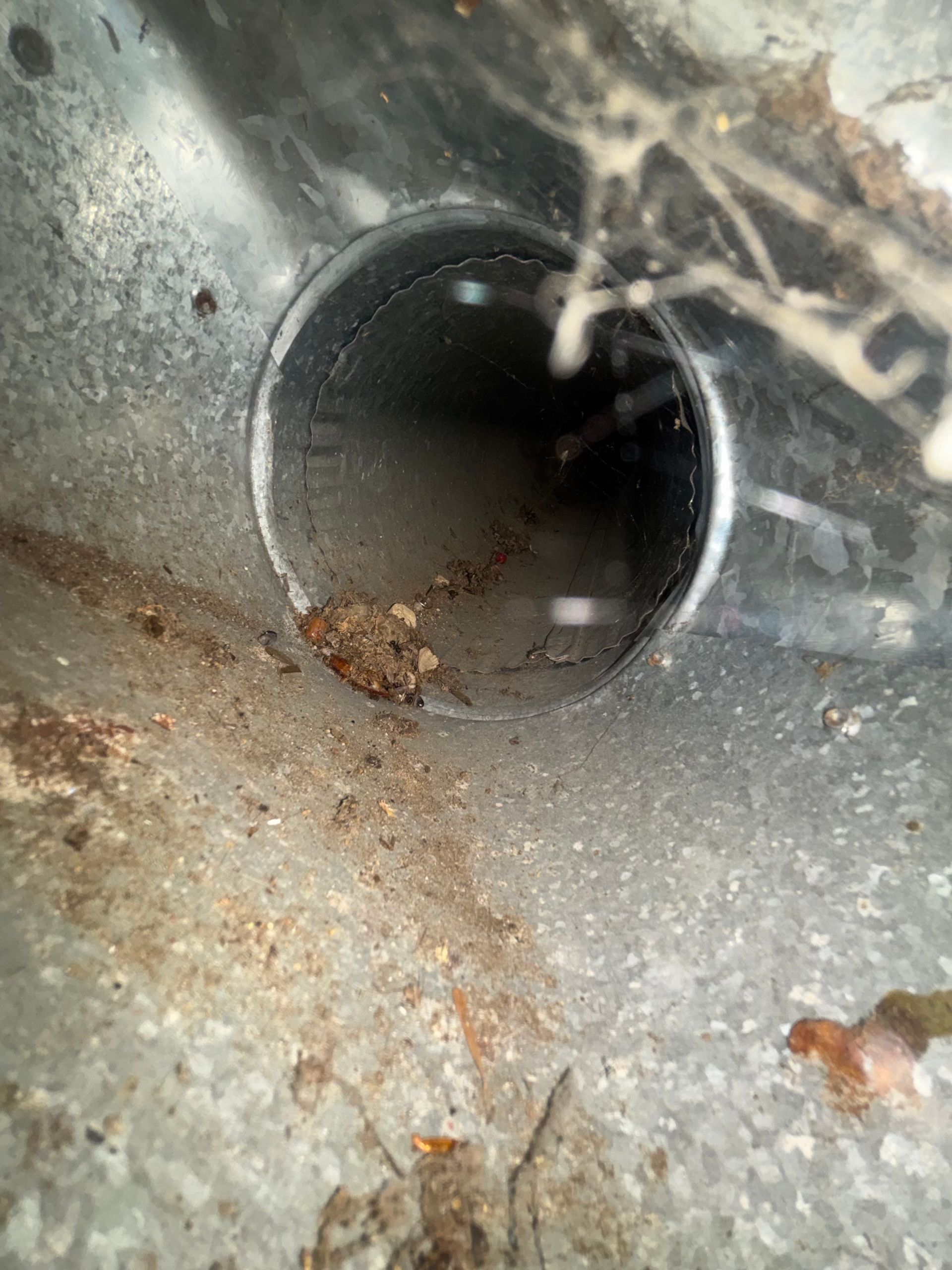 Close-up of a metal pipe opening with rust and grime inside, set against a dusty gray surface