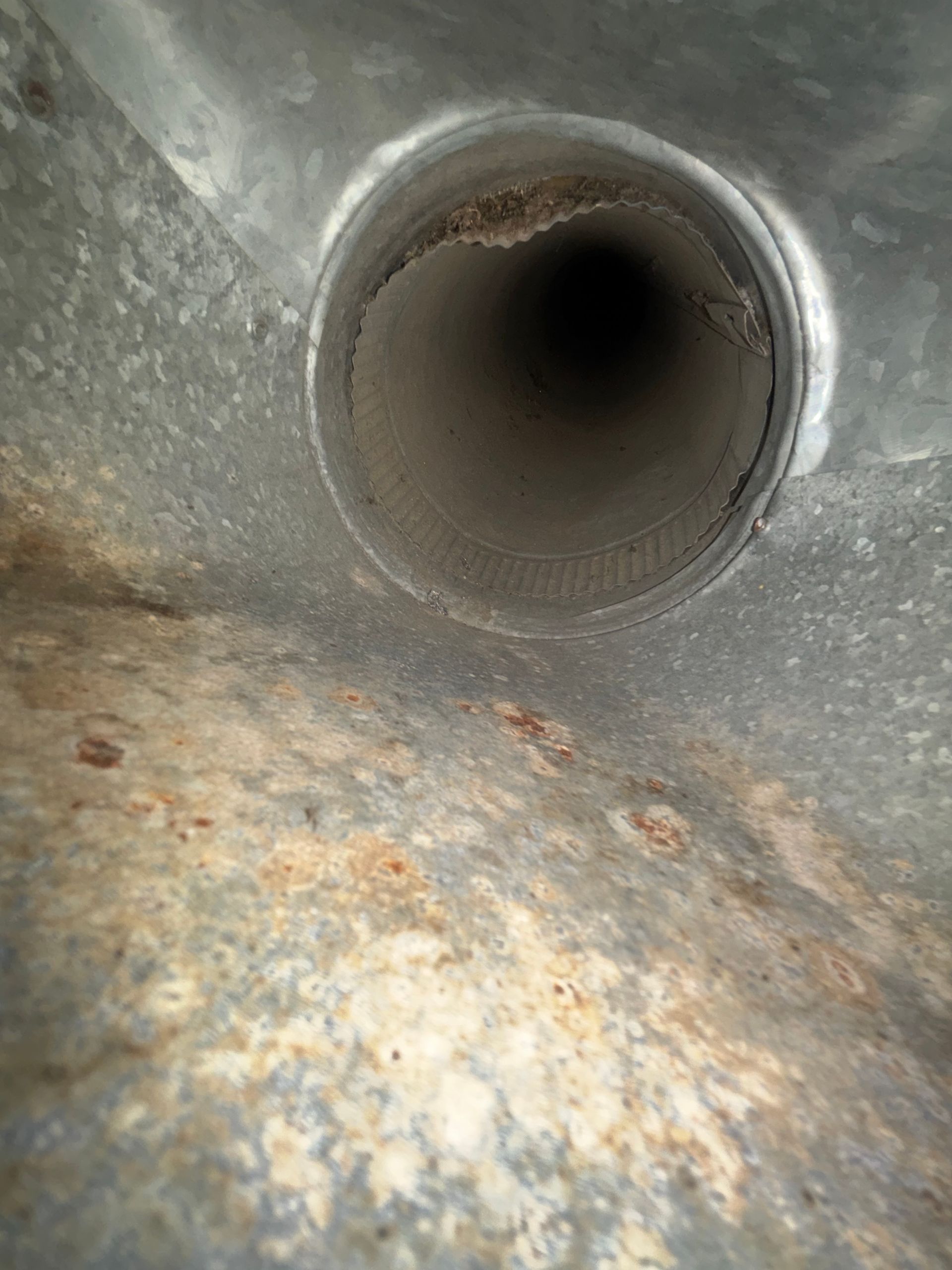 Close-up of a rusty metal pipe opening inside a corroded tank or duct.