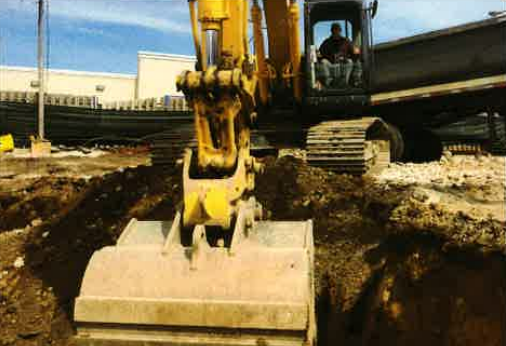 Yellow excavator digging at a construction site with a muddy trench and large bucket in foreground