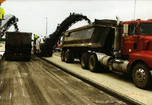 Snowy road with a red dump truck and dark dump trucks piled high with snow or debris