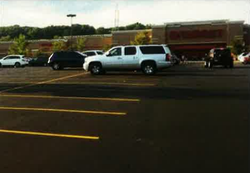 Parking lot with several cars and a white SUV in front of a red building