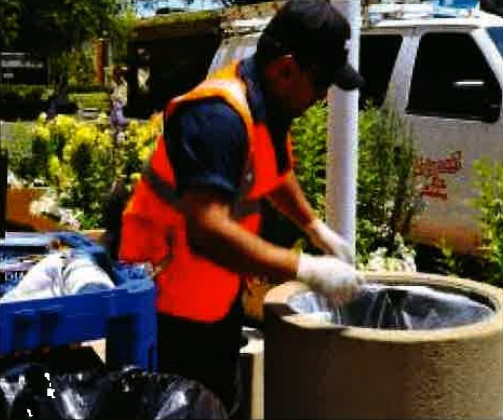 Worker in orange vest and gloves handling material in a large outdoor container near a truck.