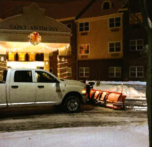 White pickup with snowplow parked outside Saint Anthony building at night in snowy street