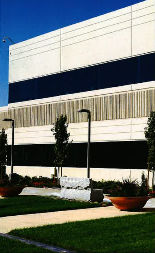Modern white building with horizontal dark windows, front lawn, and landscaped walkway under a clear blue sky