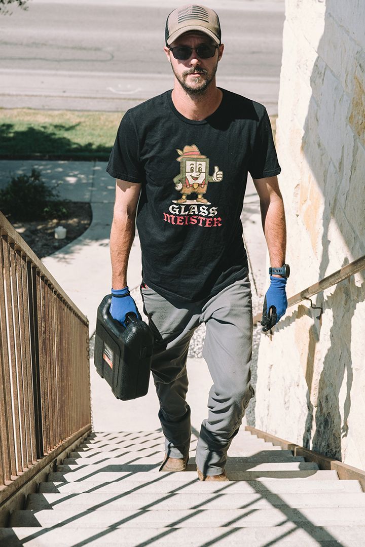 Man walking up stairs carrying a black container and a black object, wearing a t-shirt, hat, gloves, and gray pants.