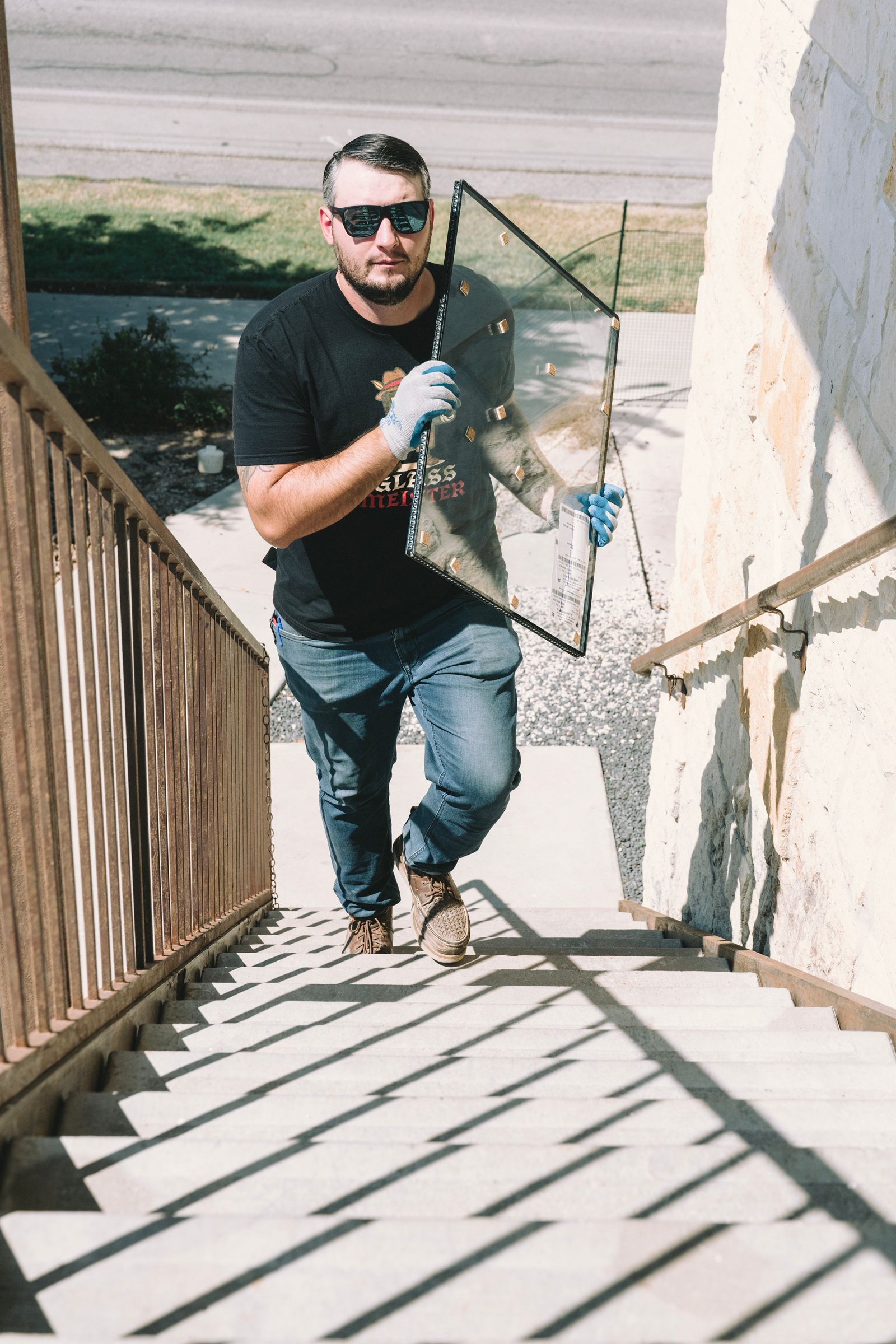 Man in sunglasses carries glass pane up outdoor stairs.