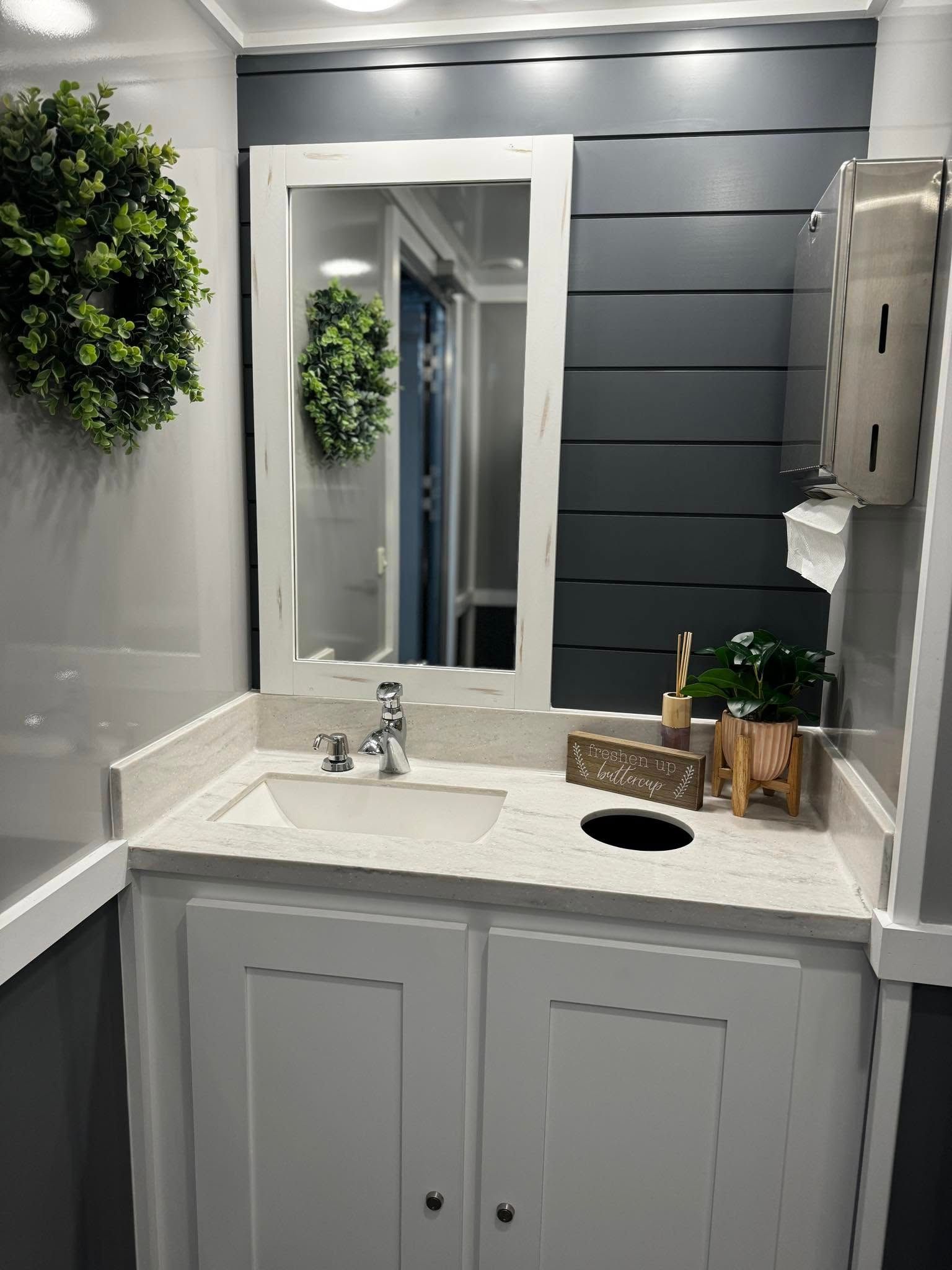 A bathroom with a sink , mirror and wreath on the wall.