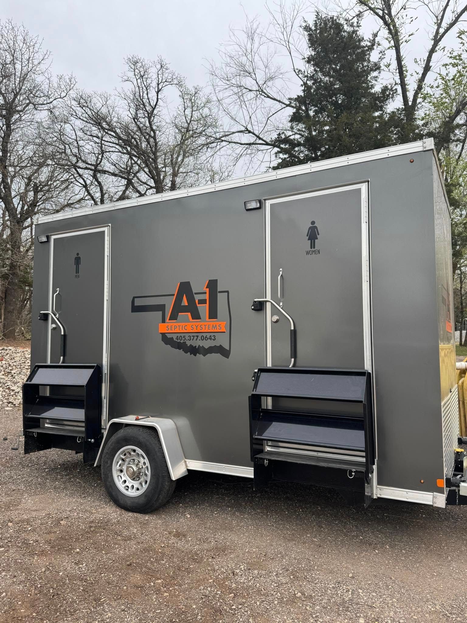 A trailer with two toilets on it is parked in a gravel lot.