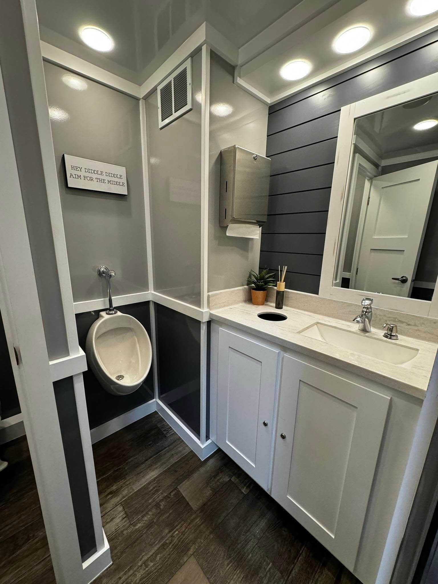 A bathroom with a urinal , sink , mirror and cabinets.