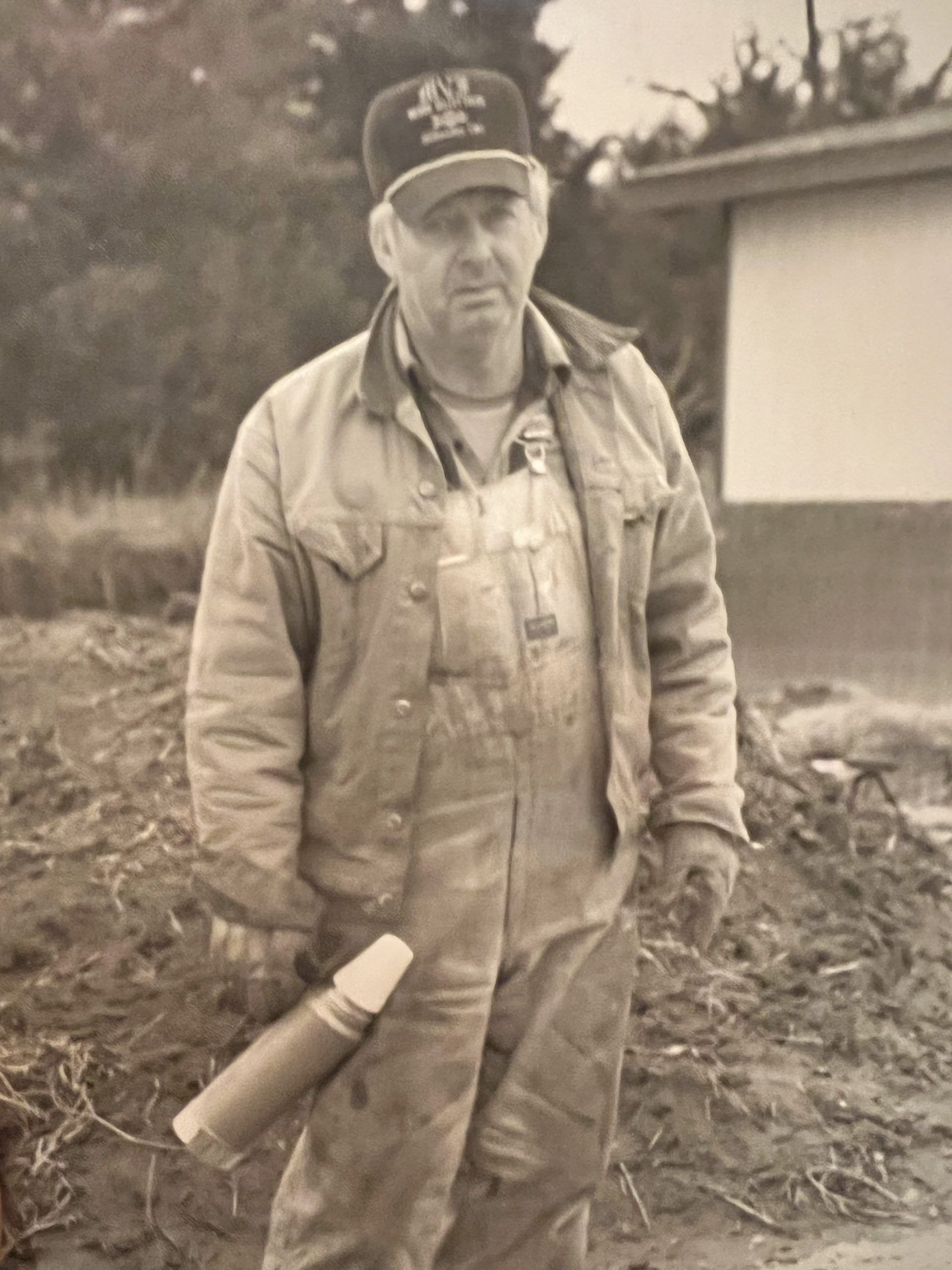 A man in overalls and a hat is holding a cane in a black and white photo.