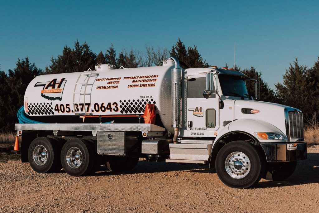 A white vacuum truck is parked in a gravel lot.