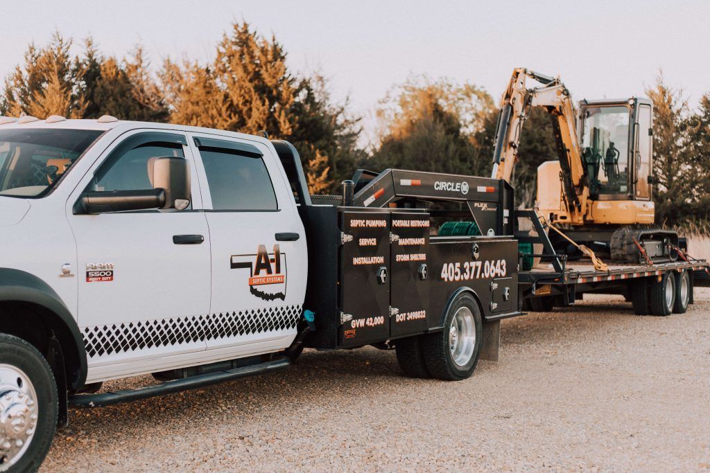 A white truck is towing a yellow excavator on a trailer.