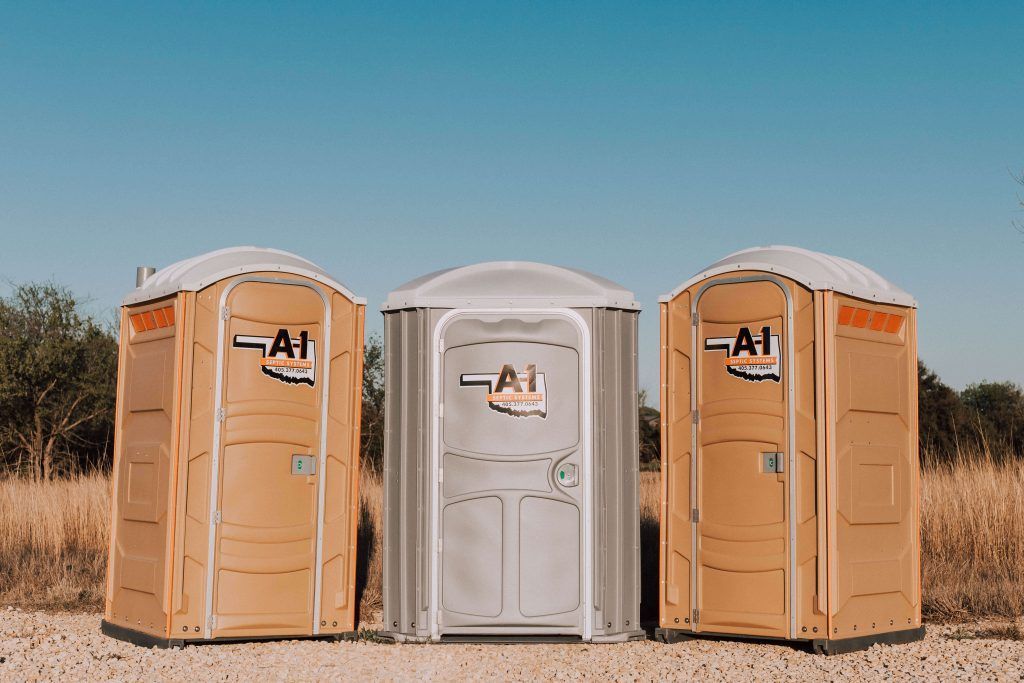Three portable toilets are lined up in a field.