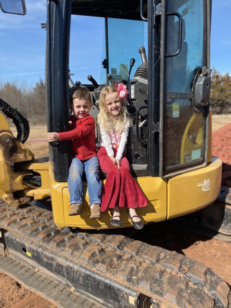A boy and a girl are sitting on the back of a bulldozer.