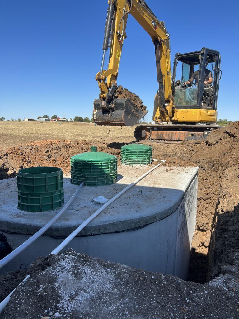 A yellow excavator is digging a hole for a septic tank