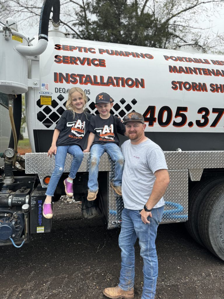 A man and two children are sitting on the back of a vacuum truck.