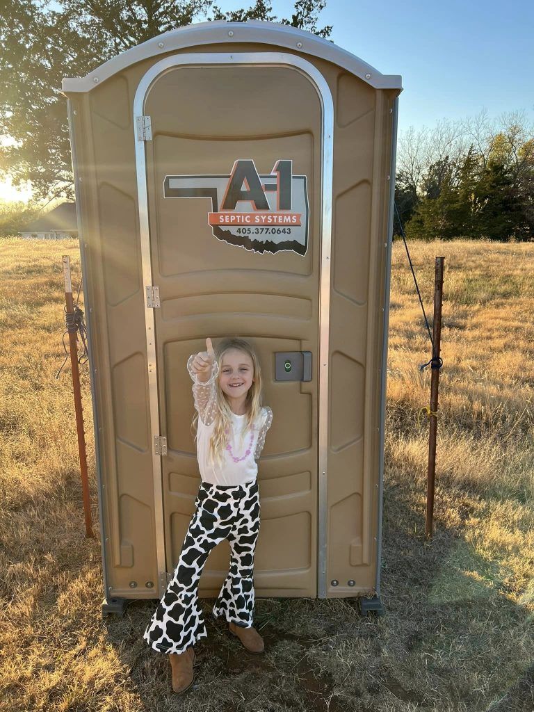A little girl is standing in front of a portable toilet in a field.
