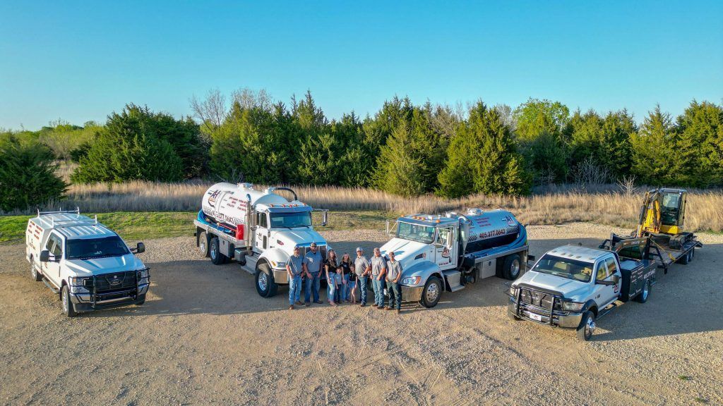 A group of people standing in front of a row of trucks in a dirt field.