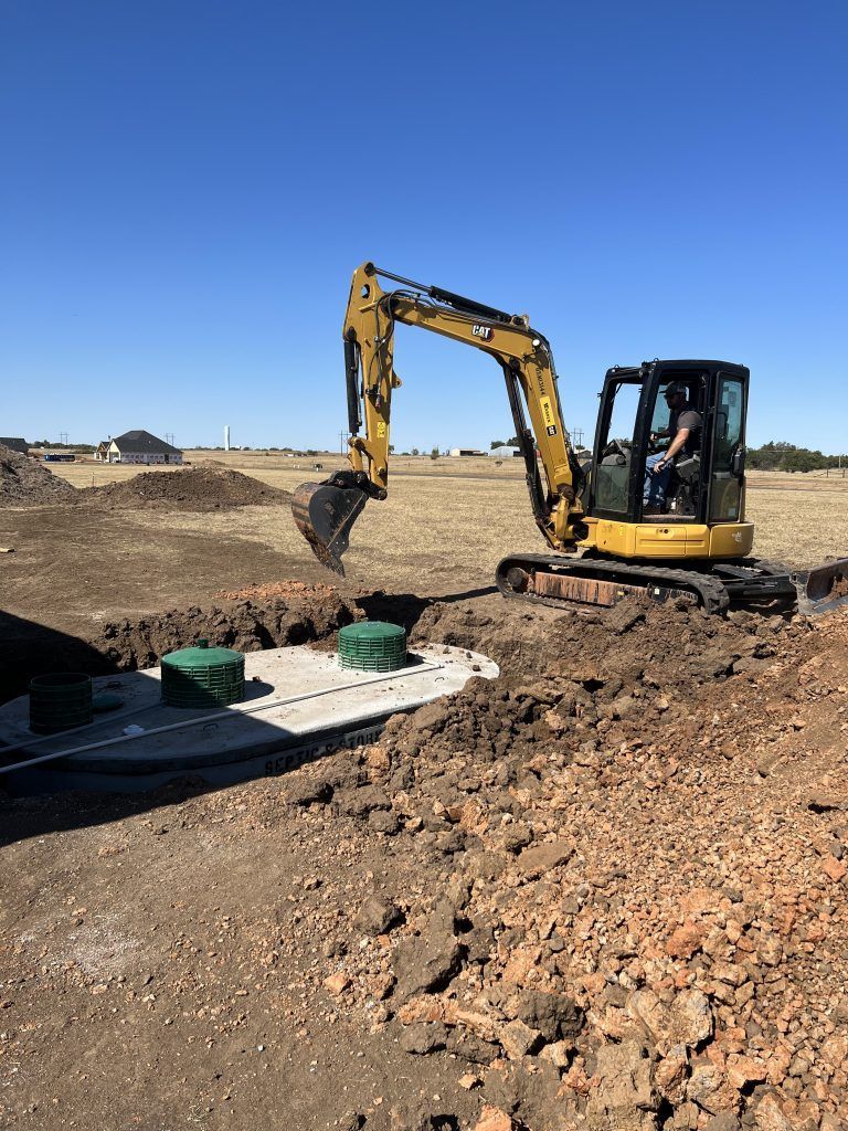 A yellow excavator is digging a hole in a dirt field.