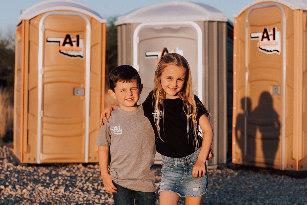 A boy and a girl are posing for a picture in front of portable toilets.