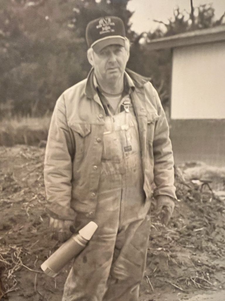 A man wearing overalls and a hat is holding a cane in a black and white photo.