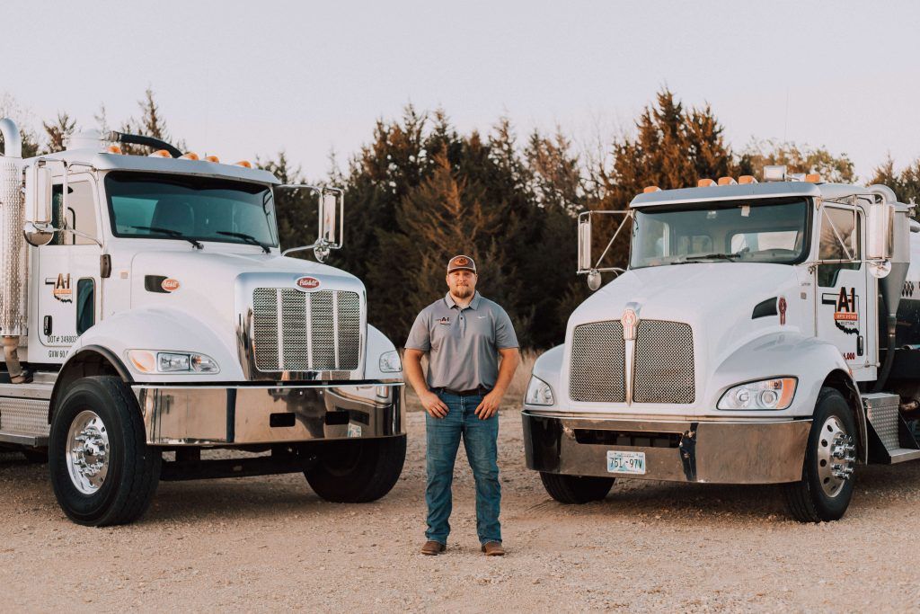 A man is standing in front of two semi trucks.