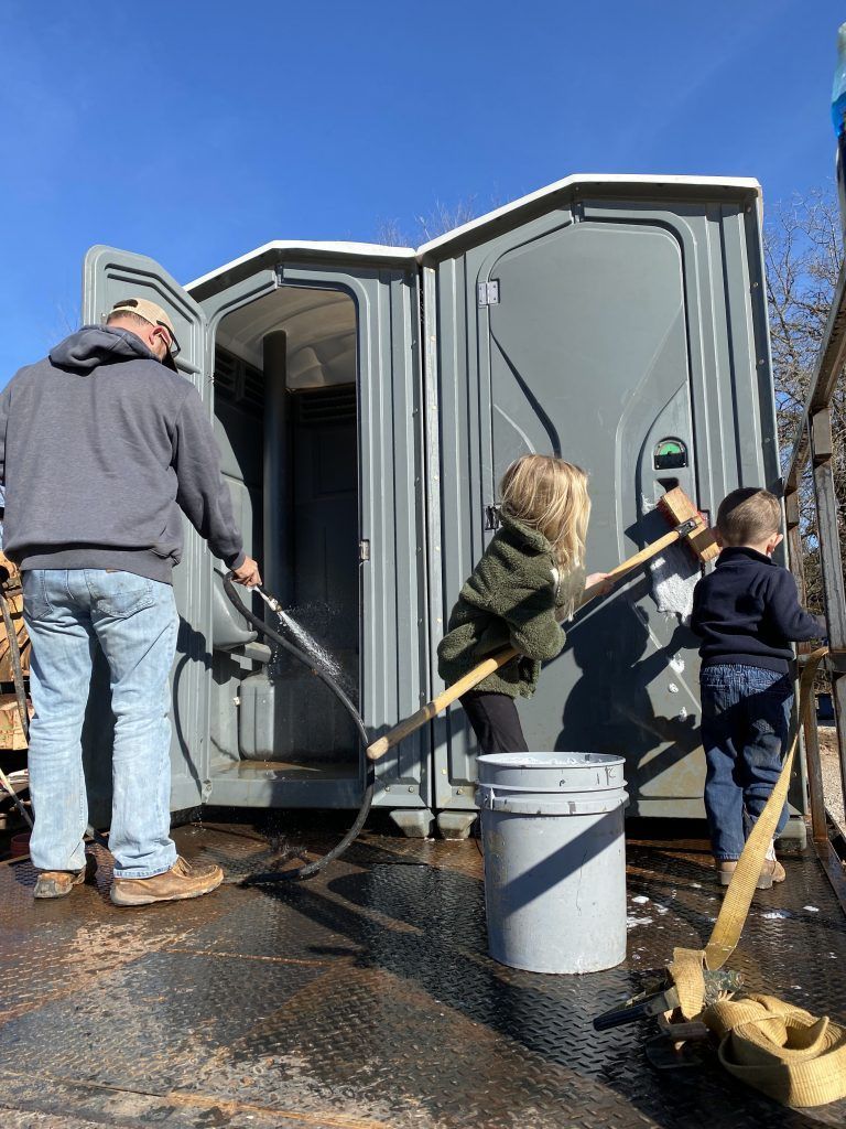 A man and two children are cleaning a portable toilet.