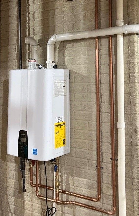 A white water heater is hanging on a brick wall next to copper pipes