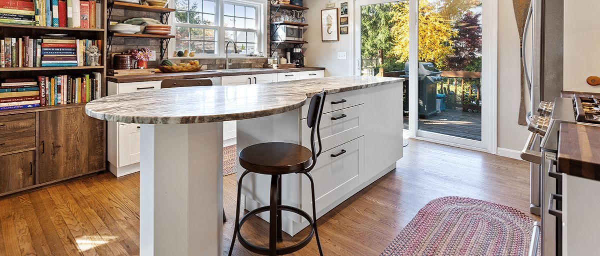 A kitchen with a large island and stools and a rug on the floor.